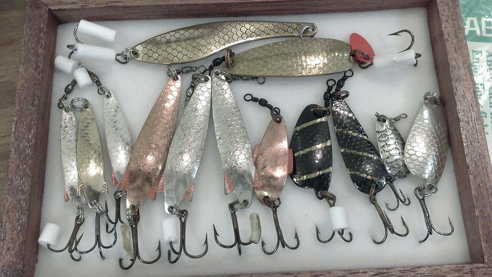 A wooden case of shiny fishing lures with hooks